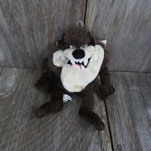 May include: Brown plush Tazmanian Devil toy with a white face and a toothy grin. The toy has a tag that says "Warner Bros."
