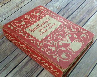 May include: A red vintage cookbook with a floral design and the title "Betty Crocker's Picture Cook Book".