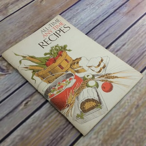 Puede incluir: Un libro de cocina vintage con una cubierta blanca e ilustraciones coloridas de comida. El título del libro es "All-Time Any Time Recipes".