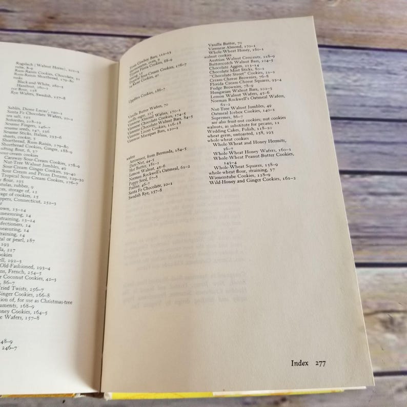 Pode incluir: Um close-up de um livro aberto com uma p&aacute;gina amarela mostrando o &iacute;ndice do livro. O &iacute;ndice lista v&aacute;rios tipos de biscoitos, incluindo manteiga de baunilha, bolachas de mel de trigo integral e biscoitos de mel selvagem e gengibre.