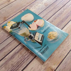 May include: A blue and white cookbook titled "Spin Cookery" with the text "Blender Cook Book" and a picture of a silver Osterizer blender with a glass jar.