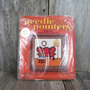 May include: A vintage needlepoint kit depicting a red living room scene with two armchairs, a small table with flowers, a lamp, and a birdcage. The kit is titled "Parlor" and is designed by Donna Kooler. The kit includes a frame, canvas, 100% wool yarn, and instructions.
