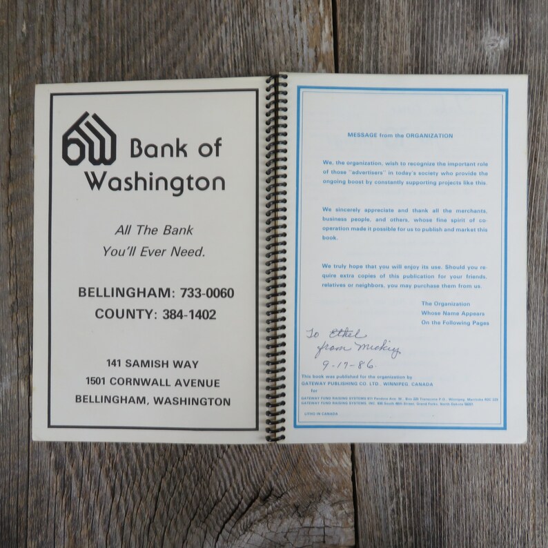 May include: A white and blue booklet with the title "Bank of Washington" and the text "All The Bank You'll Ever Need." The booklet also includes the phone numbers for Bellingham and County. The booklet is open to a page with a message from the organization and a handwritten note that says "To Ethel from Mickey 9-17-86".