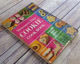 Könnte beinhalten: Ein Vintage "Woman's Day Cookie Cook Book" mit rosa Einband und farbenfrohen Illustrationen von Keksen. Das Buch enthält den Text "Over 300 Tested Recipes" und "Special: Christmas and Holiday Cookies."