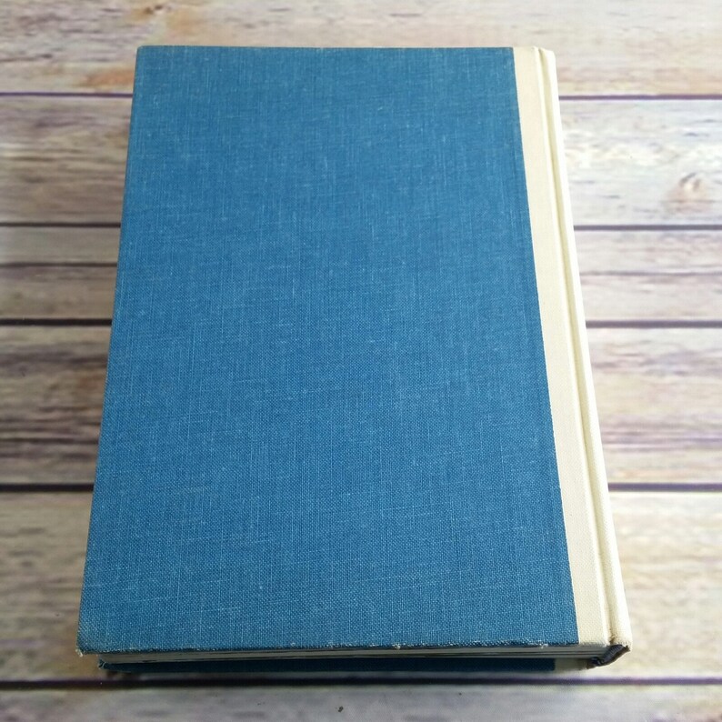 May include: A blue hardcover book with a white spine. The book is on a wooden surface.