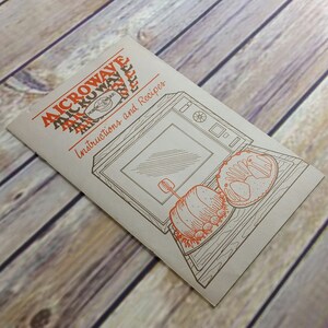 May include: A vintage microwave cookbook with instructions and recipes. The cover features a line drawing of a microwave oven with a loaf of bread and a pastry inside.