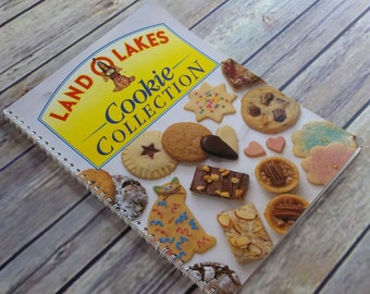 Könnte beinhalten: Ein Kochbuch mit dem Titel "Land O'Lakes Cookie Collection" mit gelbem Einband und Spiralbindung. Der Einband zeigt eine Auswahl an Keksen, darunter Zuckerkekse, Schokoladenkekse und Lebkuchen.