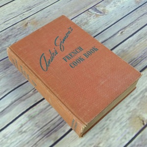 May include: A vintage orange hardback cookbook titled "Andre Simon's French Cook Book".
