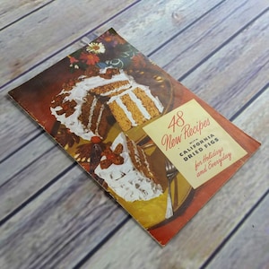 May include: A vintage cookbook with a red, white, and yellow cover featuring a photo of a cake with white frosting and a title that reads "48 New Recipes with California Dried Figs for Holidays and Everyday."