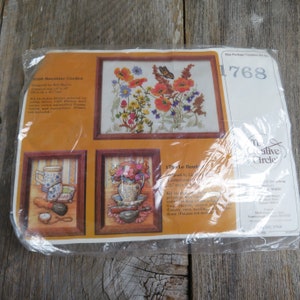 May include: A close-up of a plastic package containing two embroidery kits. The kits are titled "0308 Sunshine Garden" and "176 Le Boudoir". The package also includes the text "The Creative Circle" and the number "1768".