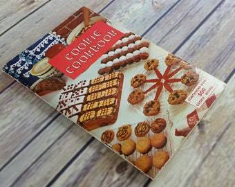 Könnte beinhalten: Ein Vintage-Kochbuch in Rot und Weiß mit dem Titel "Cookie Cookbook", das eine Auswahl an Keksen und Desserts zeigt. Das Cover zeigt eine Nahaufnahme einer Vielzahl von Keksen, darunter Schokoladenkekse, Zuckerkekse und Shortbread-Kekse. Das Kochbuch enthält über 500 Keksrezepte.