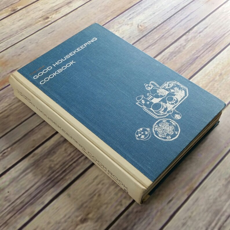 May include: A blue hardcover cookbook titled "The Good Housekeeping Cookbook". The cover features a white illustration of a tea set on a tray.