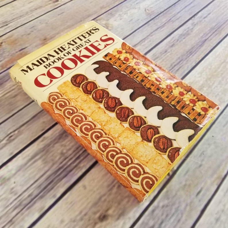 Pode incluir: Um livro de receitas vintage intitulado "Maida Heatter's Book of Great Cookies" com uma imagem colorida de v&aacute;rios biscoitos na capa.