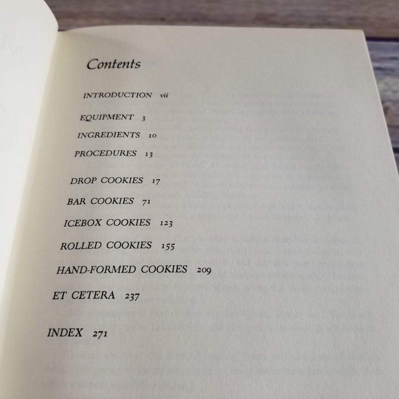 Pode incluir: Um livro intitulado "Cookies" com uma tabela de conte&uacute;do listando diferentes tipos de biscoitos, incluindo biscoitos de gota, biscoitos de barra, biscoitos de geladeira, biscoitos enrolados, biscoitos moldados &agrave; m&atilde;o e etc. O livro tamb&eacute;m inclui um &iacute;ndice.