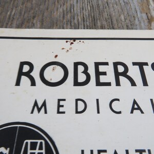 May include: A white sign with black text that reads "ROBERTS MEDICAL" with a black and white logo of a medical symbol below the text.