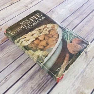 May include: A vintage cookbook titled "Farm Journal's Complete Pie Cookbook" with a photo of a pie on the cover. The cover is yellowed and worn with age. The text on the cover reads "700 Best Dessert and Main-Dish Pies in the Country."