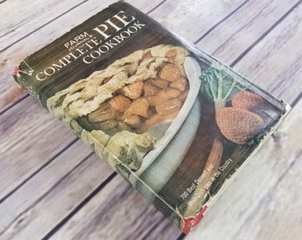 Puede incluir: Un libro de cocina vintage titulado "Farm Journal's Complete Pie Cookbook" con una foto de un pastel en la portada. La portada está amarillenta y desgastada por el paso del tiempo. El texto en la portada dice "700 Best Dessert and Main-Dish Pies in the Country."