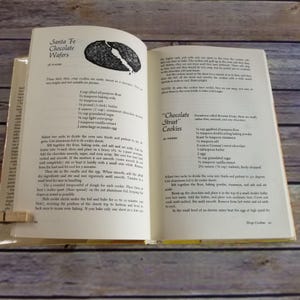 Pode incluir: Um livro de cozinha vintage aberto em duas p&aacute;ginas com receitas para "Santa Fe Chocolate Wafers" e "Chocolate Street Cookies". As receitas incluem ingredientes como manteiga, a&ccedil;&uacute;car, farinha e chocolate.