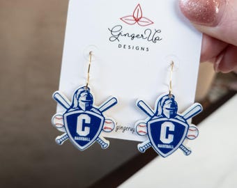 May include: Baseball earrings with a blue and white design. Each earring features a shield with a 'C' and the word 'Baseball', crossed bats, and a baseball. The earrings are on a white card with the text 'Ginger Up Designs'.