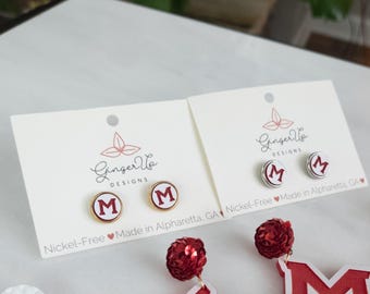 May include: Stud earrings featuring a white background and a red letter "M" in a gold or silver frame. The earrings are presented on white cards with the "Ginger Vo Designs" logo.