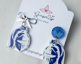 May include: Blue and white acrylic earrings with a knight's helmet design. One earring has a blue glitter stud, the other has a silver bow. The earrings are displayed on a white card with the text "Ginger Up Designs".