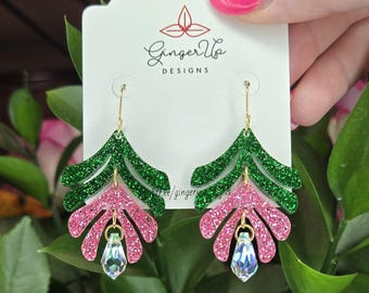 May include: Leaf-shaped earrings with green glitter tops and pink glitter bottoms. Each earring has a clear, faceted teardrop charm. The earrings hang from gold-coloured hooks. The earrings are displayed on a white card with the text "Ginger Up DESIGNS".