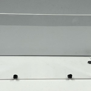 May include: Clear acrylic desktop screen with black plastic brackets. The screen is angled to provide privacy and protection from glare.