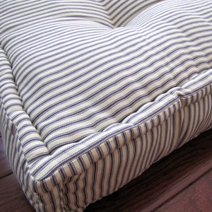 May include: A white and blue striped floor cushion with a thick, padded border. The cushion is made of a soft, durable fabric and is perfect for adding a touch of comfort to any room.