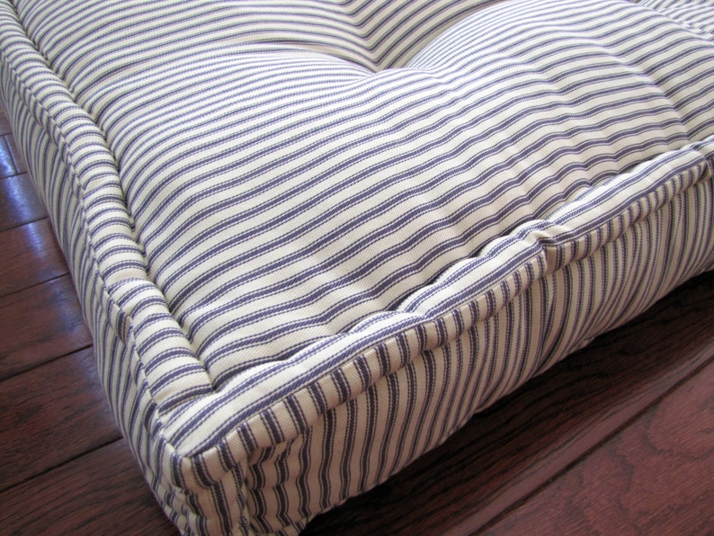 May include: A white and blue striped floor cushion with a thick, padded border. The cushion is made of a soft, durable fabric and is perfect for adding a touch of comfort to any room.