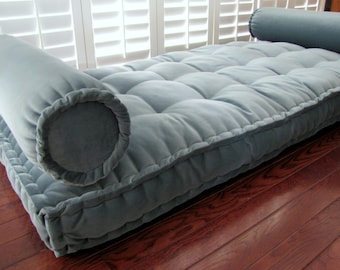May include: A light blue tufted floor cushion with two matching cylindrical pillows. The cushion is made of a soft, plush fabric and has a tufted design. The pillows are perfect for lounging and relaxing.