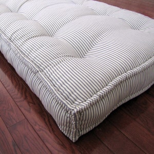 May include: A white and blue striped floor cushion with tufted buttons. The cushion has a thick, padded design and is perfect for adding comfort to any room.