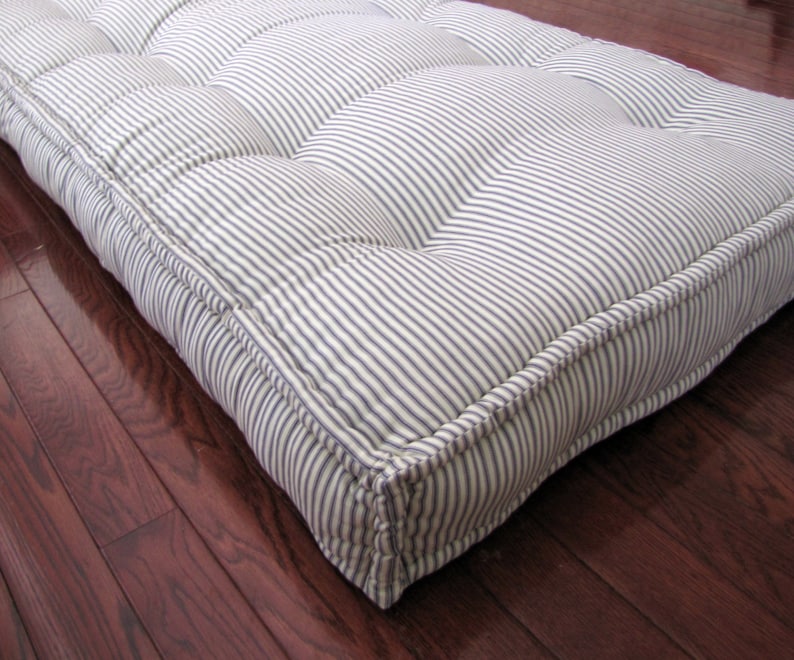 May include: A white and blue striped floor cushion with tufted buttons. The cushion has a thick, padded design and is perfect for adding comfort to any room.