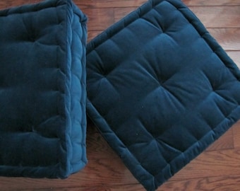 May include: Two dark blue square floor cushions with tufted tops. The cushions are made of a soft, velvety fabric.