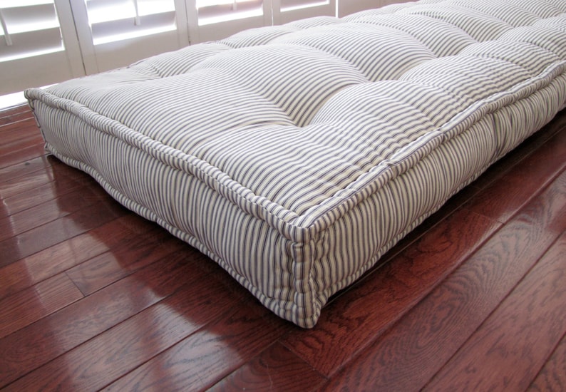 May include: A white and blue striped floor cushion with tufted detailing. The cushion is made of a soft, comfortable fabric and has a thick, supportive filling.