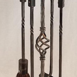 Pu&ograve; includere: Un set di attrezzi per camino in metallo nero con spazzola, poker, pala e pinze. Gli attrezzi sono montati su un supporto con un design a rotolo decorativo.