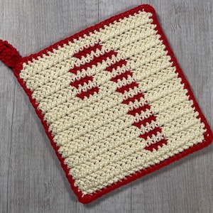 Puede incluir: Un agarrador de olla tejido a crochet con un diseño rojo y blanco. El agarrador de olla es de forma cuadrada con un asa de bucle.