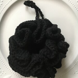 May include: Black crocheted mesh pouf with a drawstring closure. The pouf is made of a soft, textured material and is perfect for adding a touch of bohemian style to your home decor.