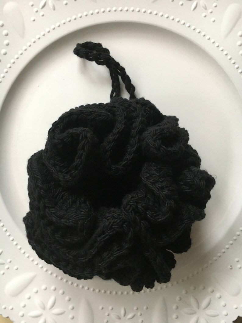 May include: Black crocheted mesh pouf with a drawstring closure. The pouf is made of a soft, textured material and is perfect for adding a touch of bohemian style to your home decor.