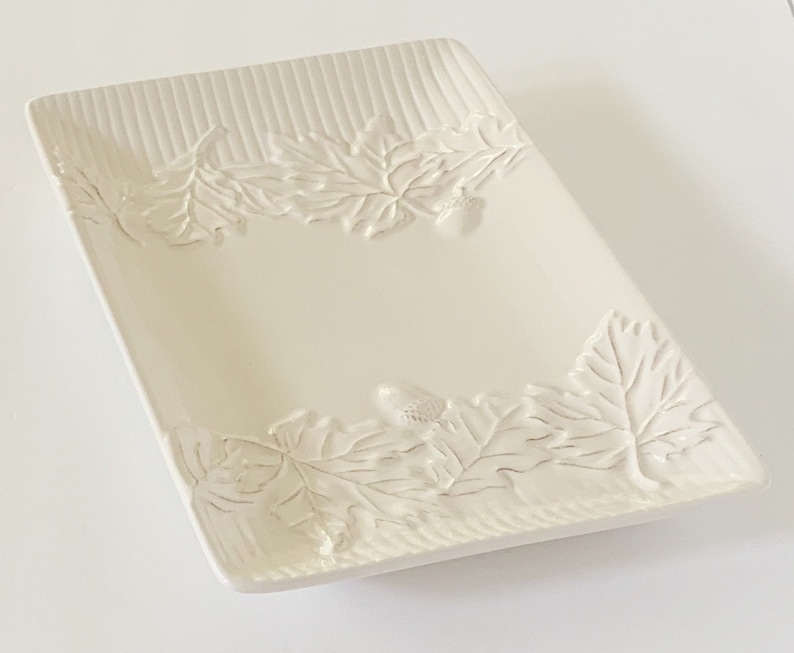 An off-white ceramic serving dish with an embossed leaf and acorn design. The dish is rectangular and has a slightly raised rim.