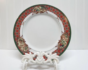 May include: A round white ceramic dinner plate featuring a decorative border with a red and green plaid pattern. The rim is accented with illustrations of woodland animals, including a pheasant and a rabbit, surrounded by colorful fruit motifs.