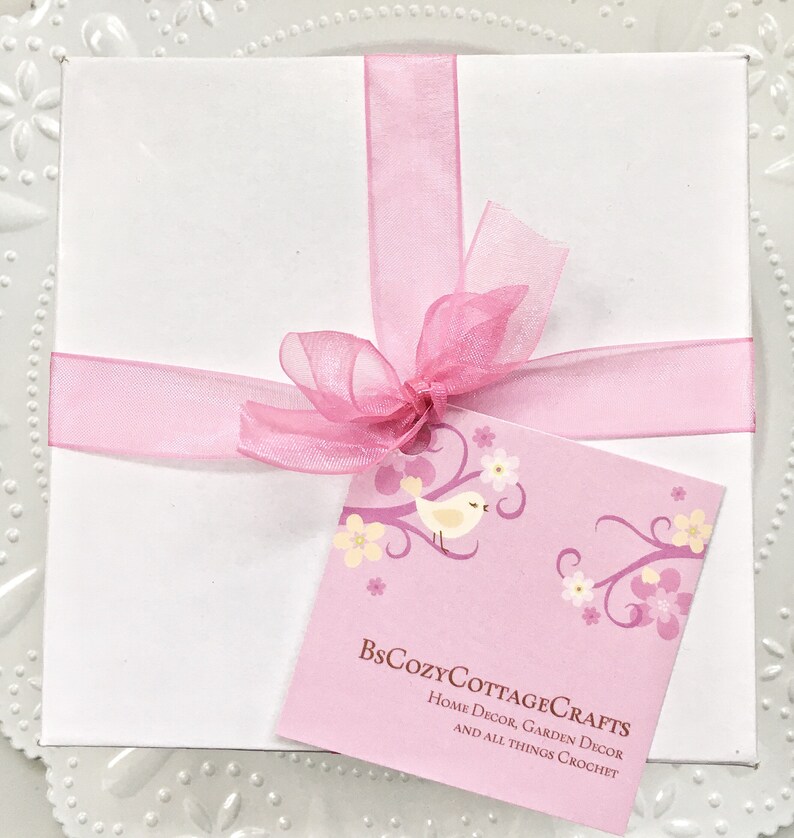 May include: A white gift box tied with a pink ribbon and bow. A pink tag with a bird and floral design is attached to the box. The tag reads "BsCozyCottageCRAFTS Home Decor, Garden Decor and all things Crochet".