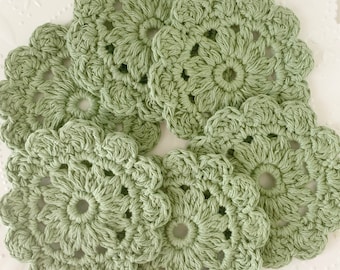 May include: Six crocheted green flower-shaped coasters. The coasters are made with a delicate, lacy pattern.