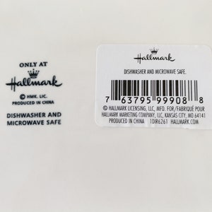 May include: A white ceramic plate with a black Hallmark logo and the text "Only at Hallmark" and "Dishwasher and Microwave Safe". The plate also has a barcode and the text "Hallmark Licensing, LLC, MFD. FOR/FABRIQU&Eacute; POUR HALLMARK MARKETING COMPANY, LLC, KANSAS CITY, MO 64141 PRODUCED IN CHINA 1DIR6261 HALLMARK.COM".