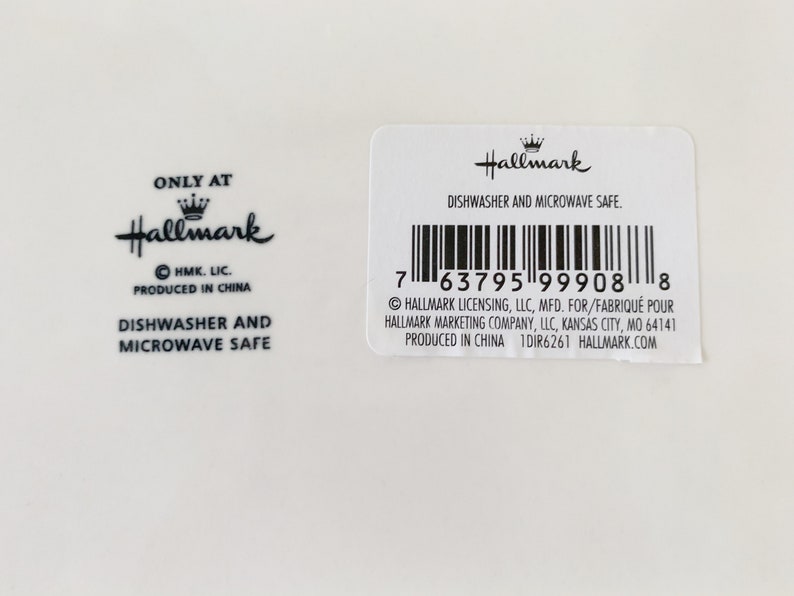 May include: A white ceramic plate with a black Hallmark logo and the text "Only at Hallmark" and "Dishwasher and Microwave Safe". The plate also has a barcode and the text "Hallmark Licensing, LLC, MFD. FOR/FABRIQU&Eacute; POUR HALLMARK MARKETING COMPANY, LLC, KANSAS CITY, MO 64141 PRODUCED IN CHINA 1DIR6261 HALLMARK.COM".