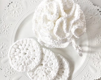 May include: White crocheted bath pouf and three round crocheted washcloths on a white lace plate.