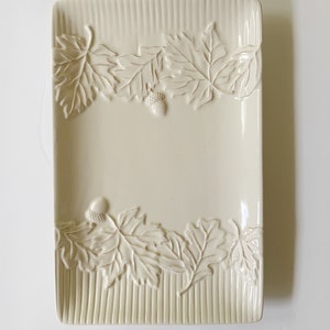 May include: A white ceramic rectangular serving dish with a raised design of leaves and acorns around the edge.