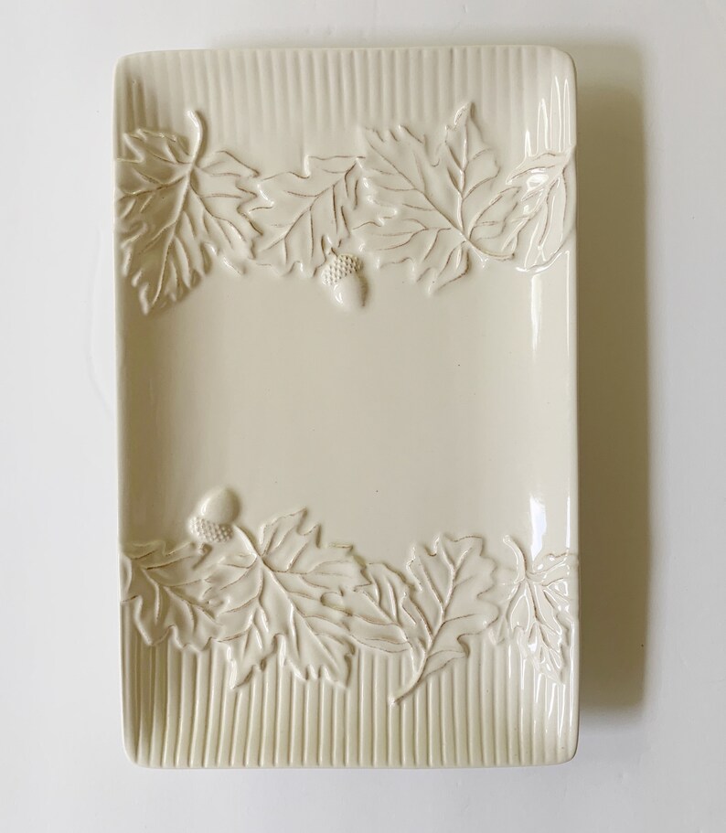 May include: A white ceramic rectangular serving dish with a raised design of leaves and acorns around the edge.