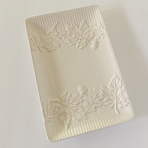 May include: A white ceramic rectangular serving dish with an embossed design of leaves and acorns around the edge.