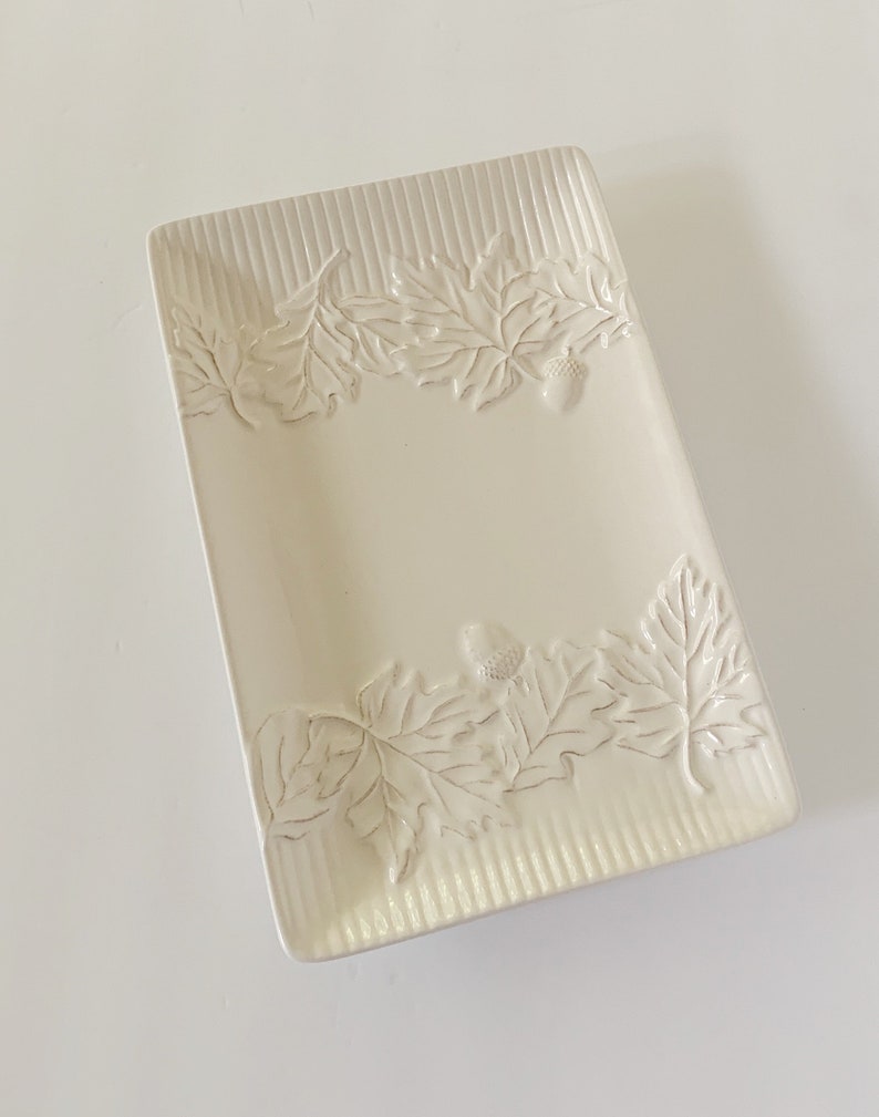 May include: A white ceramic rectangular serving dish with an embossed design of leaves and acorns around the edge.