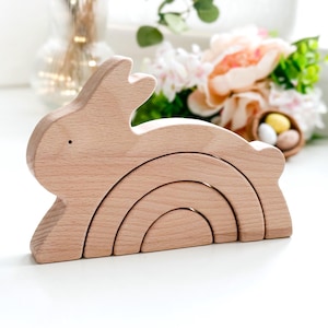 May include: A wooden toy rabbit with a rainbow arch design. The toy is made of natural wood and is perfect for stacking and playing.